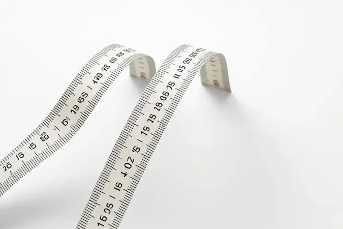 Render 3D conceitual com três fitas de trena de larguras diferentes em paralelo comparando rigidez e legibilidade.